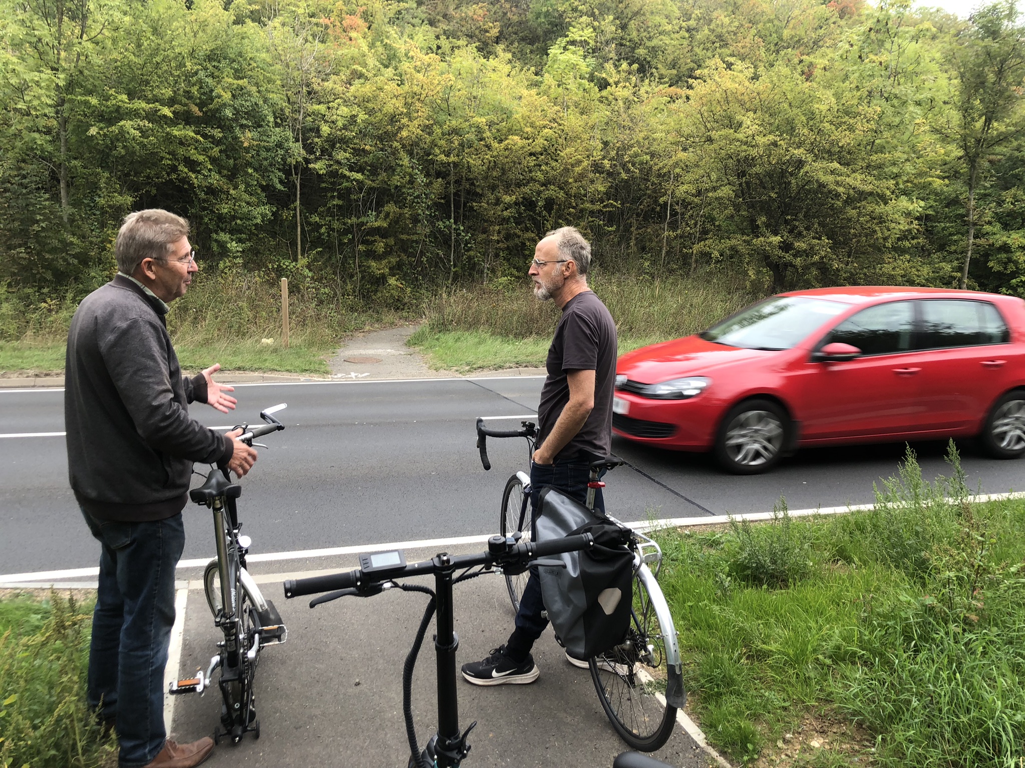 Two men standing with bikes talking at the side of busy country road